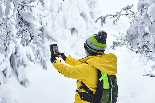 Frauenreisende mit Rucksack in einem verschneiten Winterwald macht Selfie