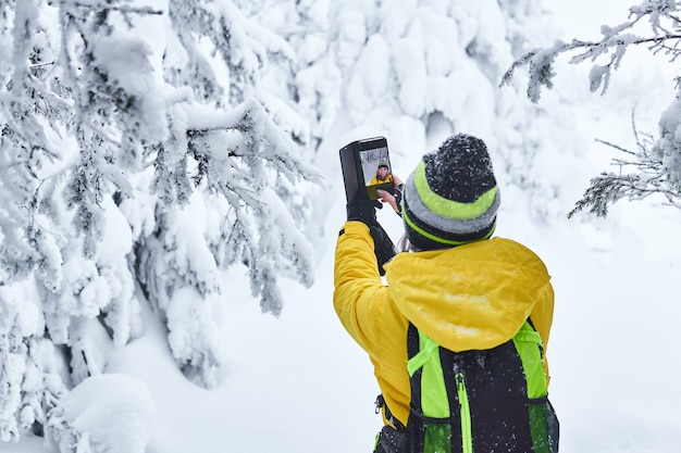 Frauenreisende mit Rucksack in einem verschneiten Winterwald nimmt Videos mit sich selbst per Smartphone auf