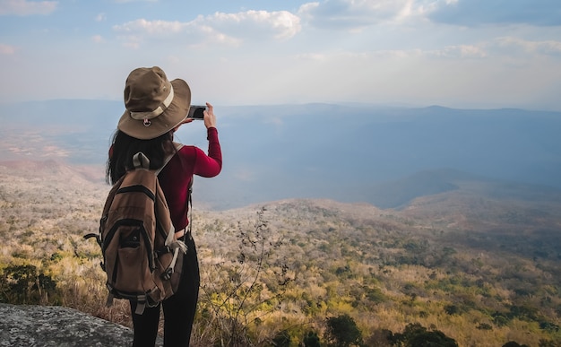 Frauenreisender, der oben auf dem berg steht und fotoansicht der natur im urlaub nimmt.