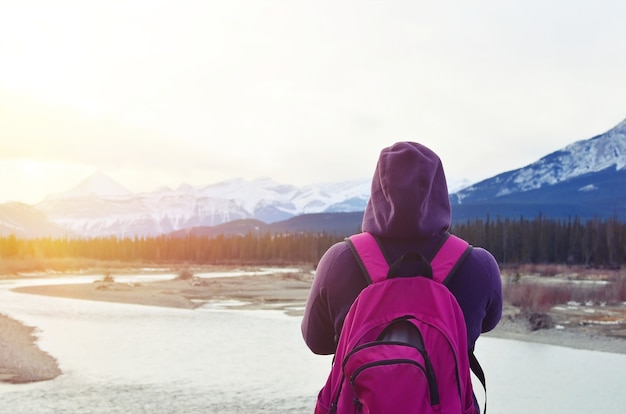 Frauenreisender mit dem Rucksack, der erstaunliche Berge mit Schnee und Wald betrachtet