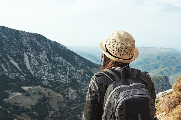 Frauenreisender mit Hut, der auf einem Hintergrund grüner Berge steht