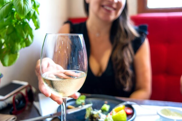 Frauenschattenbild, das ein Glas weiße Rebe in einer Restauranthandansicht hält