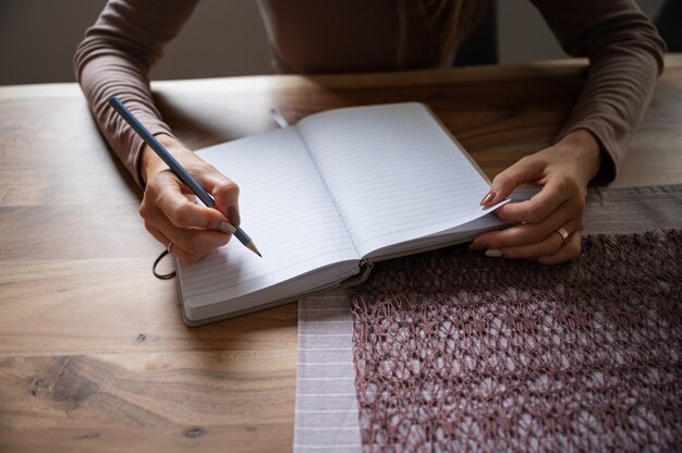 Foto frauenschreiben in leerem notizblock mit einem bleistift auf hölzernem esstisch. konzeptionell von zu hause aus zu arbeiten oder zu studieren.