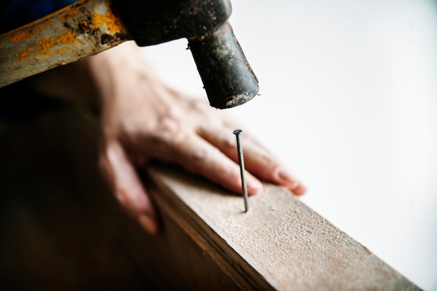 Frauentischler, der den hammer drückt nagel auf einem holz verwendet