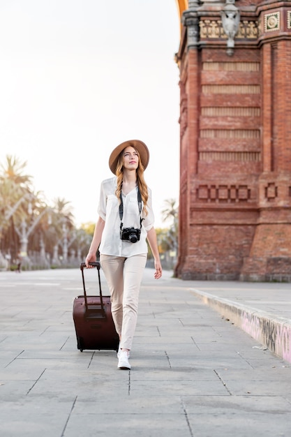 Frauentourist, der durch die Stadt geht, die einen Koffer und eine Vintage-Kamera trägt.