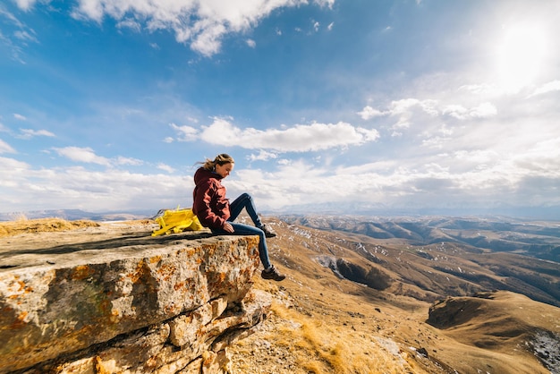 Frauentourist sitzt am Rand einer Klippe im Hintergrund der Berge