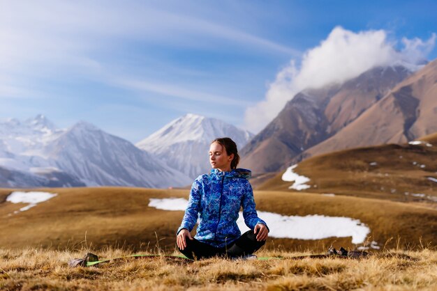 Frauentourist sitzt auf dem Hintergrund der Berge und praktiziert Yoga