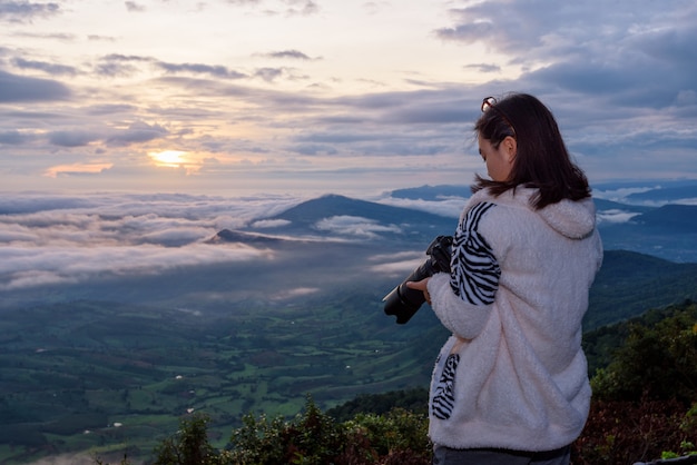 Frauentouristen schauen in die Kamera, nachdem sie ein Foto auf der Naturlandschaft des Sonnennebels und der Berge während des Sonnenaufgangs im Nationalpark Phu Ruea, Provinz Loei, Thailand gemacht haben