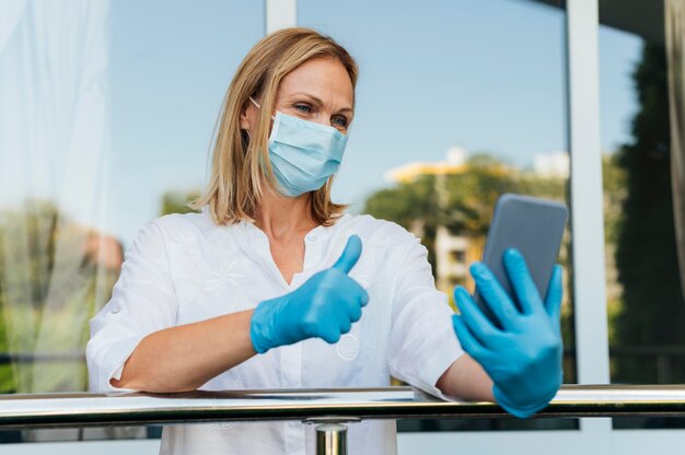 Frauenvideoanruf von zu Hause mit medizinischer Maske und Handschuhen