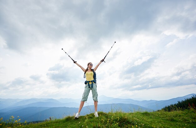 Frauenwanderer, der auf grasbewachsenem Hügel mit Trekkingstöcken in den Bergen wandert