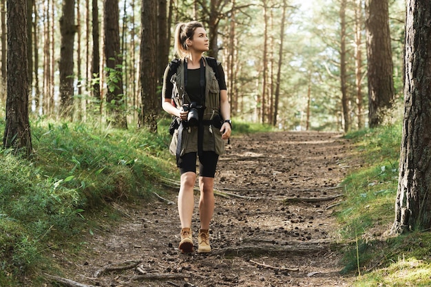 Frauenwanderer, die mit einem Rucksack und einer modernen spiegellosen Kamera im grünen Wald spazieren gehen