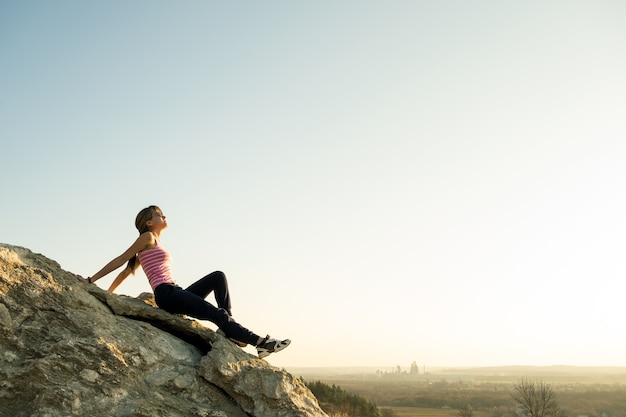Frauenwanderer sitzen auf einem steilen großen Felsen und genießen einen warmen Sommertag.