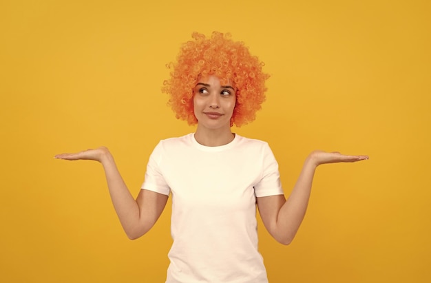 Freaky mujer con peluca de payaso que presenta el producto expresa emociones positivas chica divertida con peluca naranja