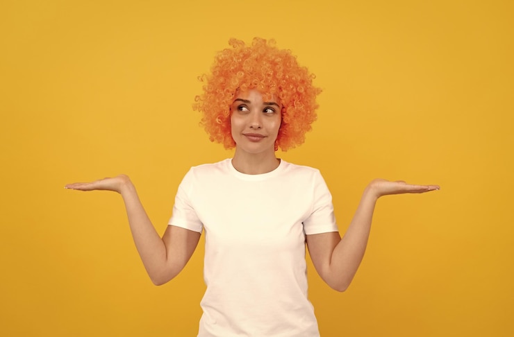 Foto freaky mujer con peluca de payaso que presenta el producto expresa emociones positivas chica divertida con peluca naranja