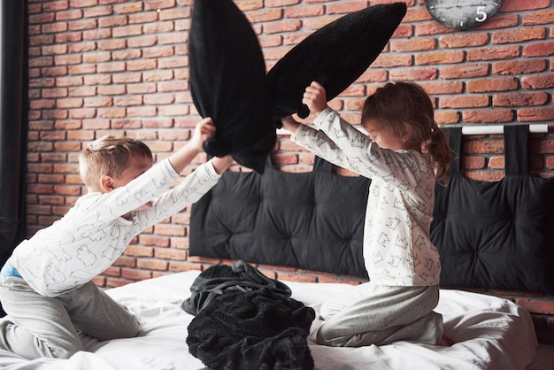 Freche Kinder Kleiner Junge und Mädchen veranstalteten eine Kissenschlacht auf dem Bett im Schlafzimmer. Sie mögen diese Art von Spiel