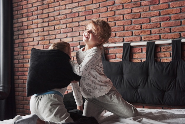 Freche Kinder Kleiner Junge und Mädchen veranstalteten eine Kissenschlacht auf dem Bett im Schlafzimmer. Sie mögen diese Art von Spiel