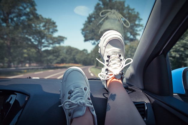 Freedom Car Travel-Konzept - Frau, die sich mit den Füßen auf dem Armaturenbrett entspannt und weiße Turnschuhe trägt.