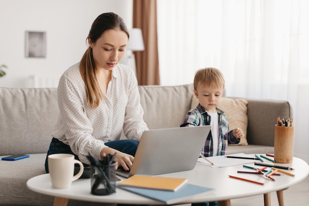 Freelance e licença maternidade jovem mãe trabalhando em laptop em casa e cuidando dela