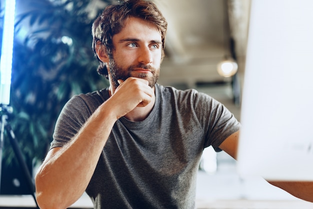 Freelance hombre barbudo usando la computadora en un lugar de coworking moderno. Concepto de negocio independiente