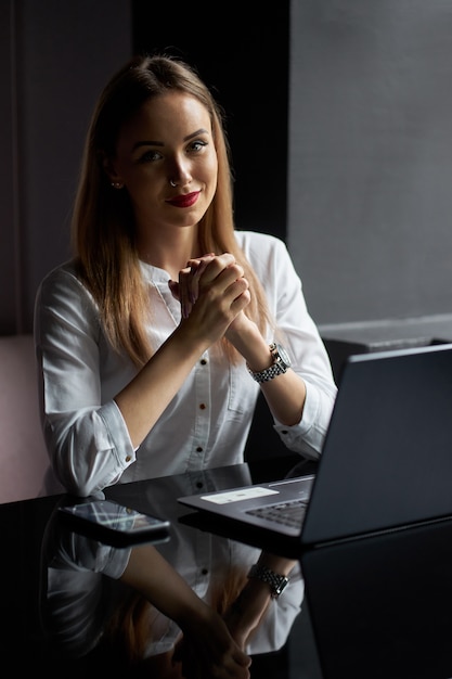 Freelance en el lugar de trabajo. Joven rubia hermosa mujer empresario vistiendo blusa blanca trabajando con el portátil en una cafetería.