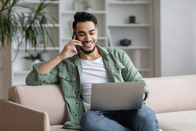 Freelance masculino árabe de negocios remotos hablando por teléfono y usando una computadora portátil