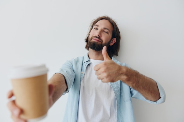 Freelance-Millennial-Mann mit Bart, der Kaffee aus einer recycelten Tasse trinkt, in stilvoller Hipster-Kleidung, weißem T-Shirt, blauen Jeans und Hemd auf weißem Hintergrund. Hochwertiges Foto