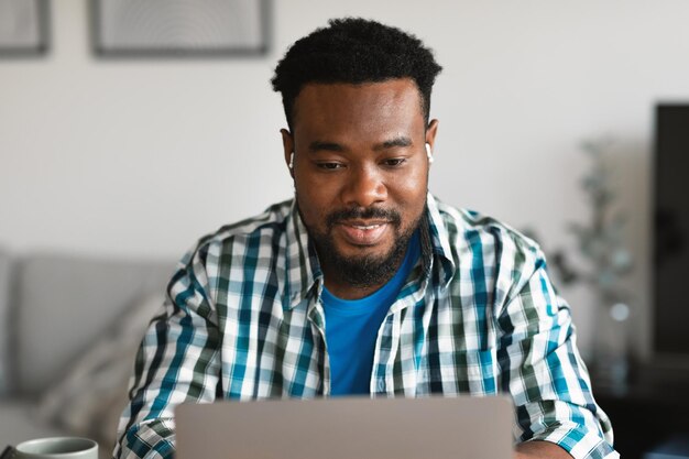 Freelancer afro-americano usando laptop usando fones de ouvido em casa