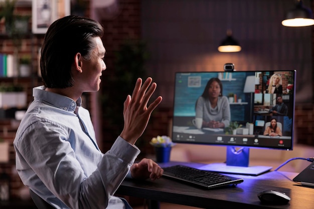 Freelancer asiático acenando para conferência de videochamada com webcam, participando de reunião de teleconferência on-line no computador. Conversando com a pessoa em chamada de videoconferência remota, tendo conversa de teletrabalho.