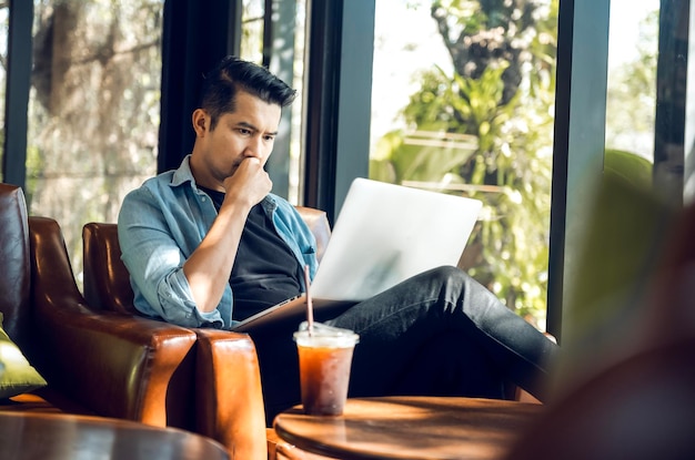 Freelancer asiático en blazer con computadora portátil en café cerca de la ventana Profesión es traductor y escritor independiente de blogger Traductor independiente trabaja en aprendizaje en línea de cafetería