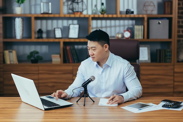 Freelancer asiático graba podcasts de audio El empresario trabaja en la oficina usa un micrófono profesional y una computadora portátil