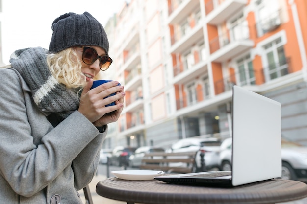 Freelancer del blogger de la mujer joven en café al aire libre con la computadora, teléfono móvil.