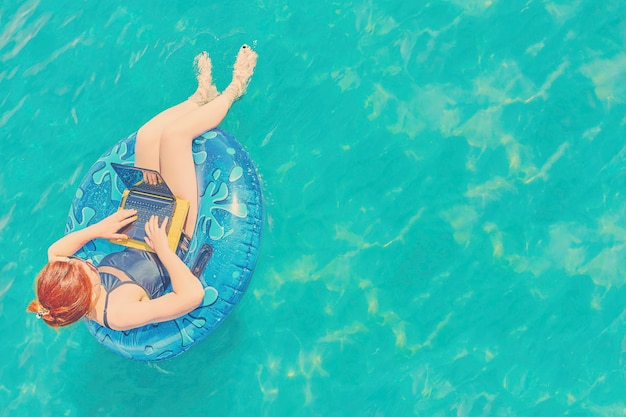 El freelancer bonito joven de la mujer está flotando en el mar o en la piscina en un círculo de la natación