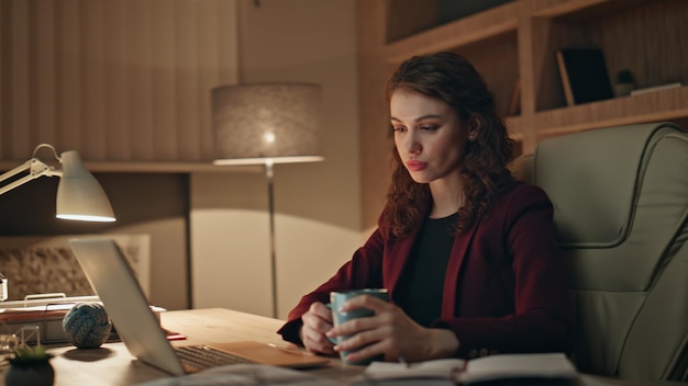 Freelancer cansado desfrutar de café trabalhando horas extras no escritório laptop à noite de perto