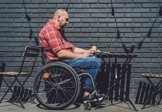 Freelancer com deficiência física em uma cadeira de rodas, trabalhando em um café de rua