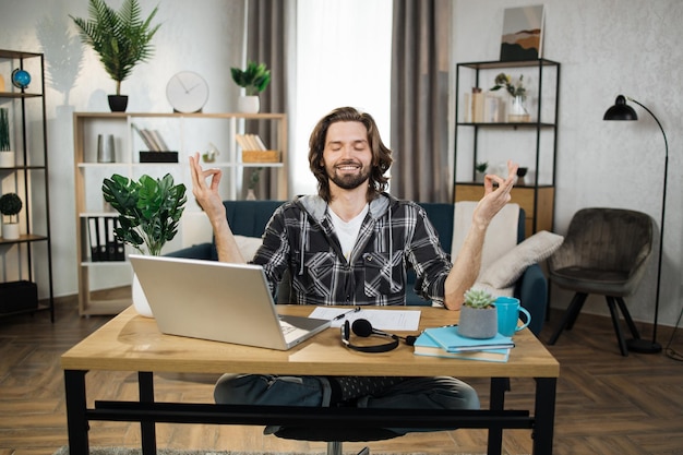 Foto freelancer de homem em óculos sentado à mesa com os olhos fechados e aliviando o estresse pela meditação