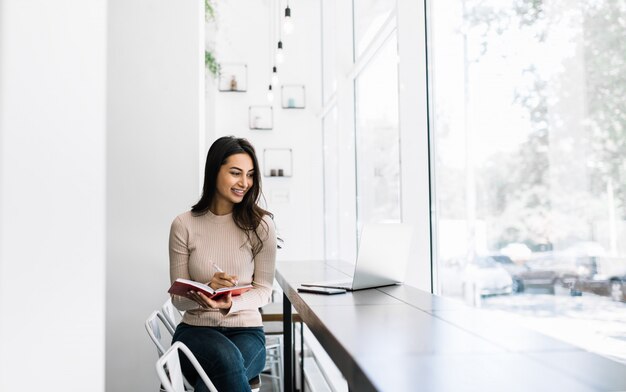 Freelancer de linda mulher indiana usando laptop, escrevendo notas, trabalhando em casa. Estudante asiática estudando, preparação para exames, ensino a distância