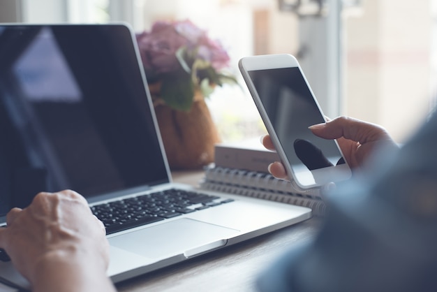 Foto freelancer de mulher de negócios usando telefone celular, trabalhando em um computador laptop em um escritório moderno