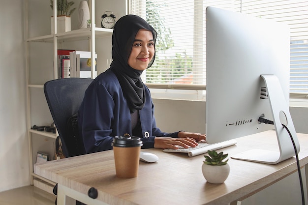 Freelancer de mulher muçulmana feliz trabalhando ou conversando com clientes no computador, sentado no escritório.
