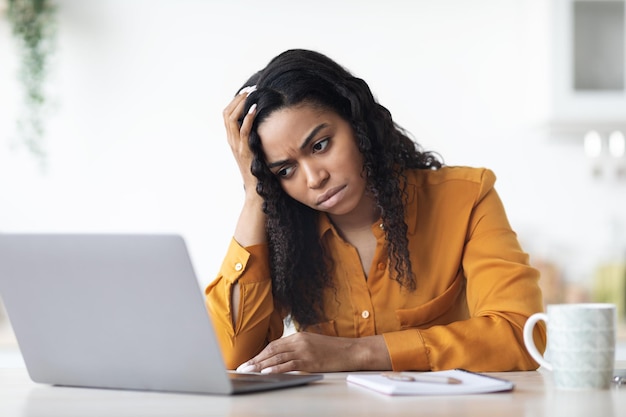 Freelancer de senhora negra chateada trabalhando no laptop em casa