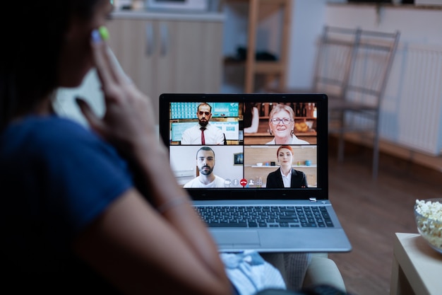 Freelancer em videoconferência à noite com a equipe sentada no sofá usando um laptop