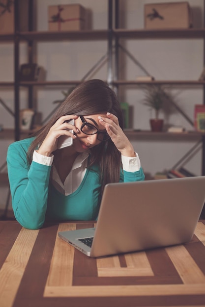 Freelancer está trabajando con algo y sentado en la mesa con una computadora portátil y hablando por teléfono