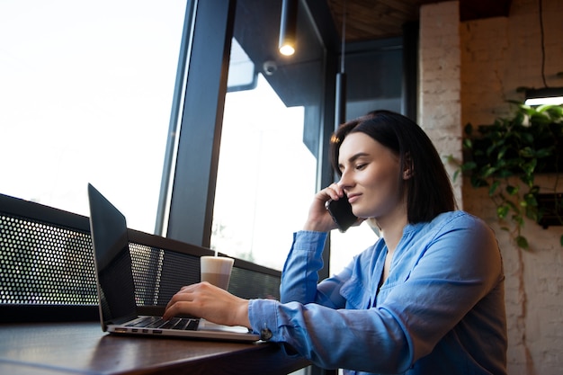 Freelancer feminina a falar alegremente ao telefone durante o trabalho remoto no portátil