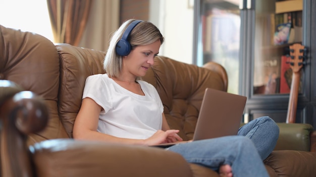 Freelancer feminina com fones de ouvido e laptop trabalha online enquanto está sentada no sofá mulher fazendo