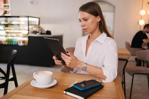 Freelancer feminina trabalhando em café usando tablet digital jovem gerente de negócios bebe café durante