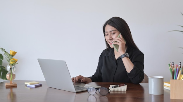 Freelancer feminino conversando com telefone celular e usando laptop