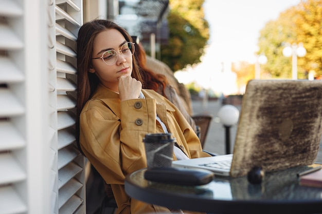 Freelancer feminino pensativo tocando o queixo e olhando para a tela do laptop enquanto pensa no projeto