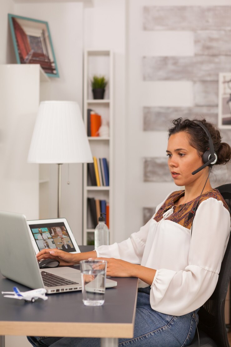 Foto freelancer feminino usando fones de ouvido durante uma videochamada trabalhando em casa.