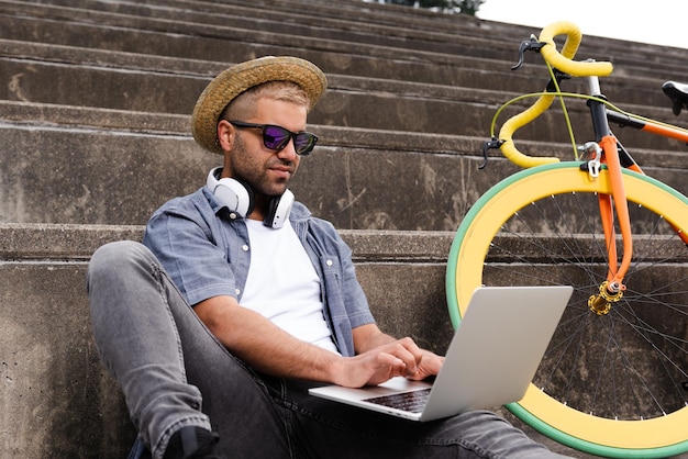 Freelancer hipster hispânico trabalhando em seu laptop ao ar livre ao lado de uma bicicleta colorida