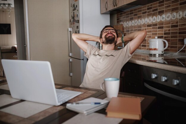 Freelancer hipster sonriente tomados de la mano detrás de la cabeza sentado en el escritorio de la oficina detrás de la computadora portátil