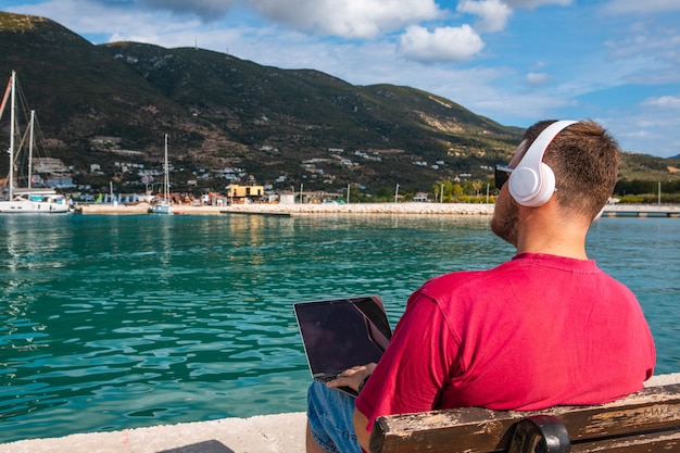 Freelancer hombre trabajando en un portátil en el verano del banco del puerto de la ciudad